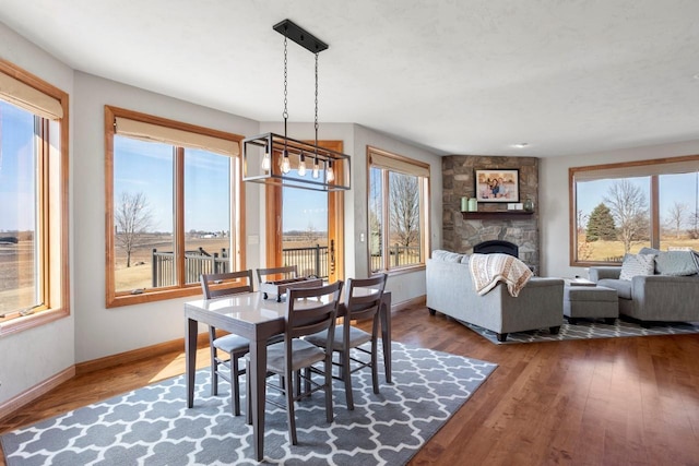 dining room featuring a stone fireplace, an inviting chandelier, baseboards, and wood finished floors