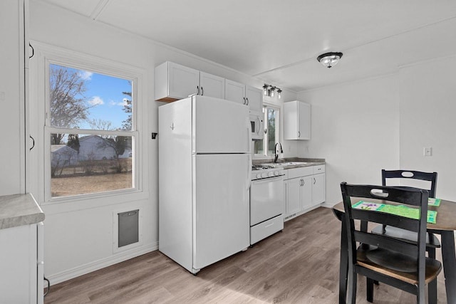 kitchen with a healthy amount of sunlight, white appliances, white cabinetry, and light wood-style floors