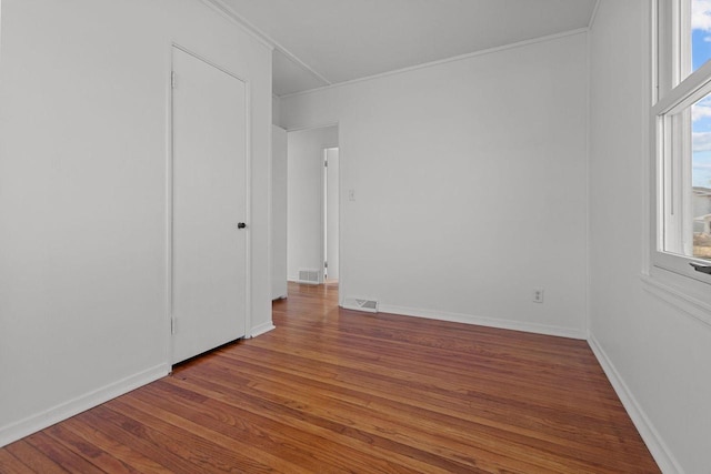 spare room with crown molding, wood finished floors, visible vents, and baseboards