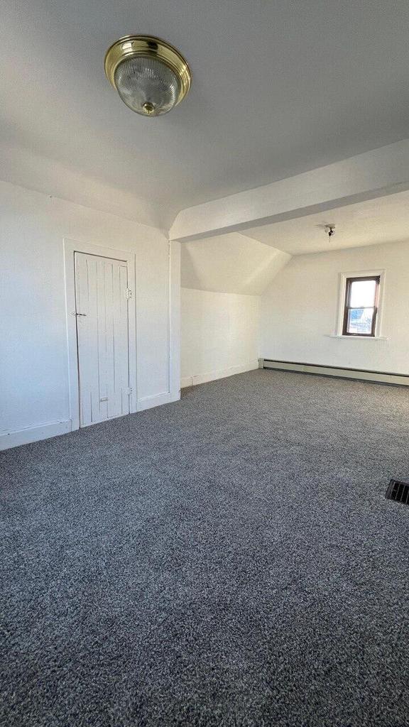 carpeted empty room featuring visible vents, a baseboard heating unit, and vaulted ceiling