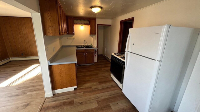 kitchen featuring brown cabinets, a sink, wood finished floors, white appliances, and light countertops