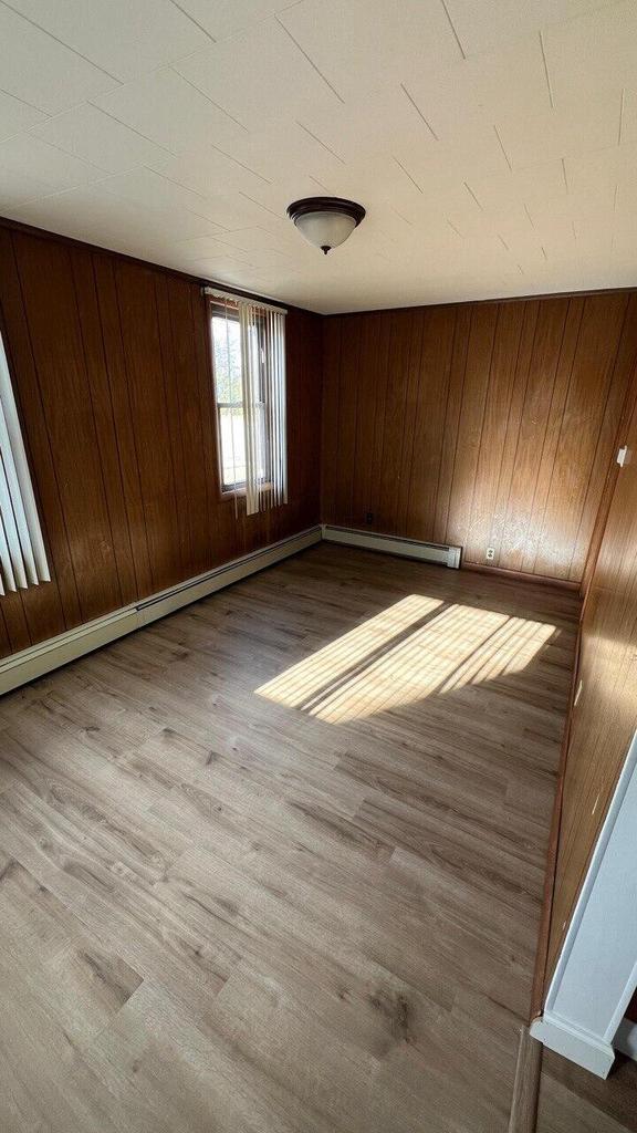 unfurnished room with wooden walls, wood finished floors, baseboards, and a baseboard radiator