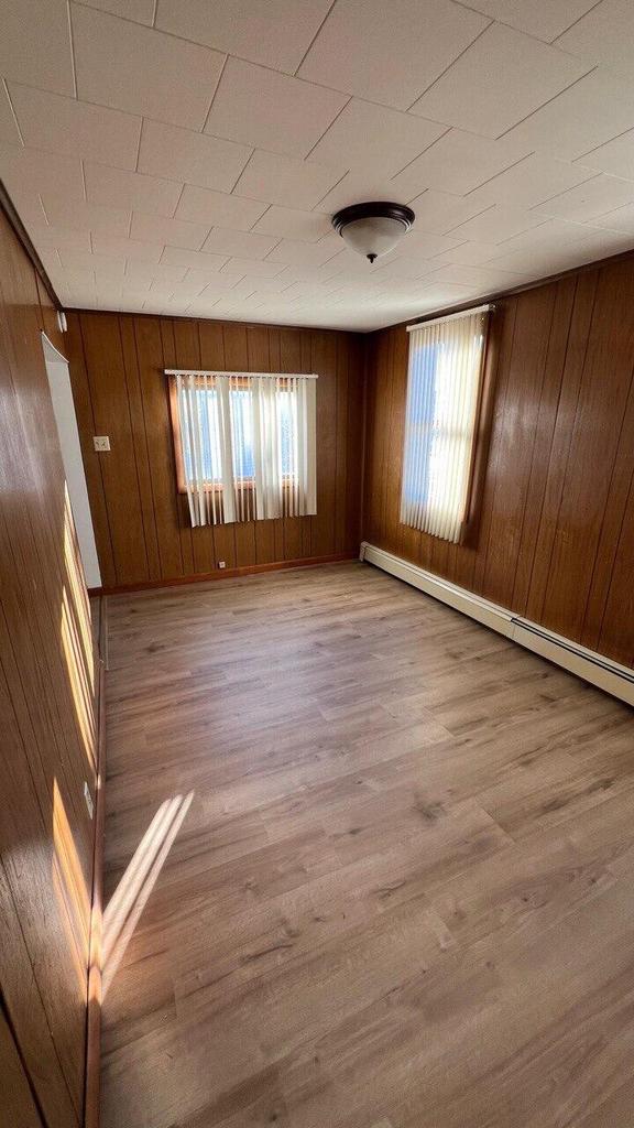 empty room featuring wooden walls, wood finished floors, a wealth of natural light, and a baseboard radiator