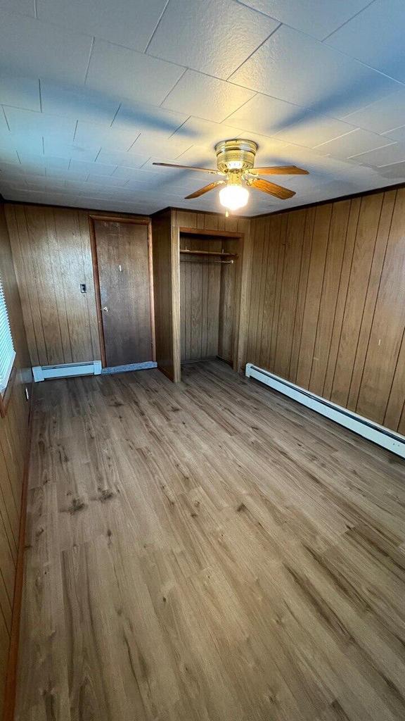 unfurnished bedroom with wood walls, a baseboard heating unit, and wood finished floors