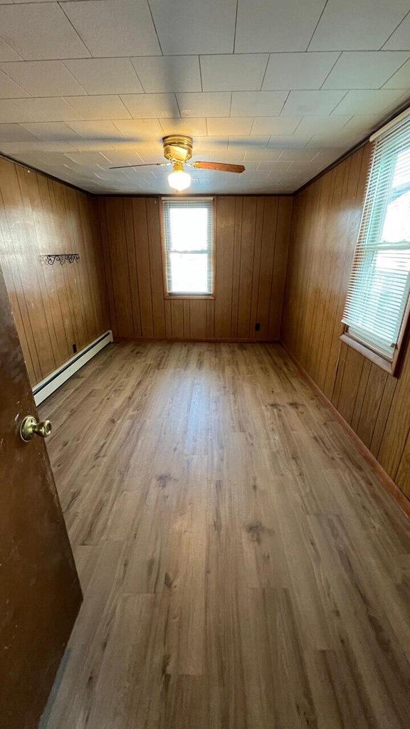 spare room with a baseboard radiator, wood walls, and light wood finished floors