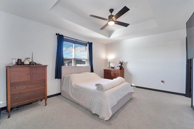 bedroom featuring a ceiling fan, a raised ceiling, light colored carpet, and baseboards