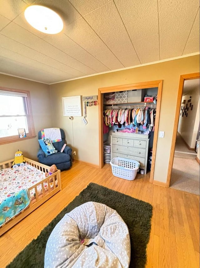 bedroom with a closet, baseboards, crown molding, and hardwood / wood-style flooring