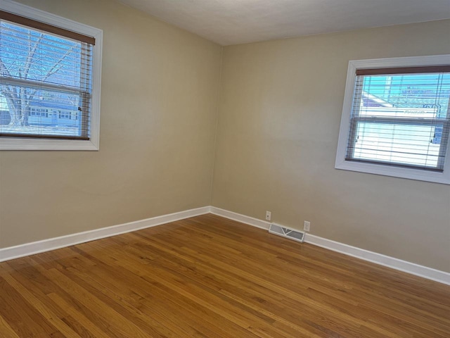 empty room featuring wood finished floors, baseboards, and visible vents