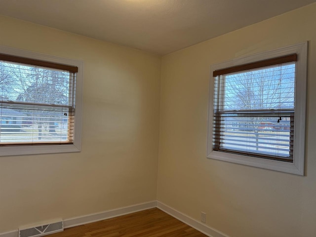 empty room with wood finished floors, baseboards, and visible vents