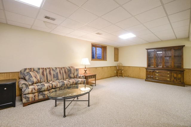 carpeted living area with a drop ceiling, a wainscoted wall, visible vents, and wood walls