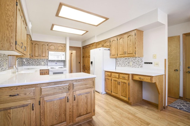 kitchen featuring white appliances, a peninsula, a sink, light countertops, and light wood-style floors