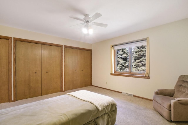 bedroom featuring visible vents, multiple closets, light carpet, baseboards, and ceiling fan