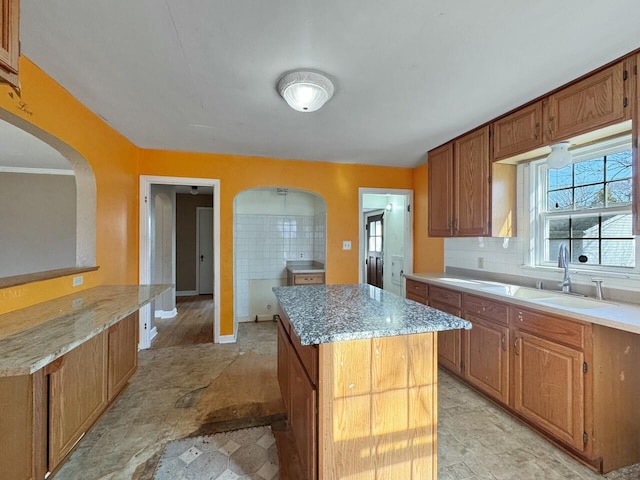 kitchen with light stone counters, arched walkways, backsplash, and a kitchen island