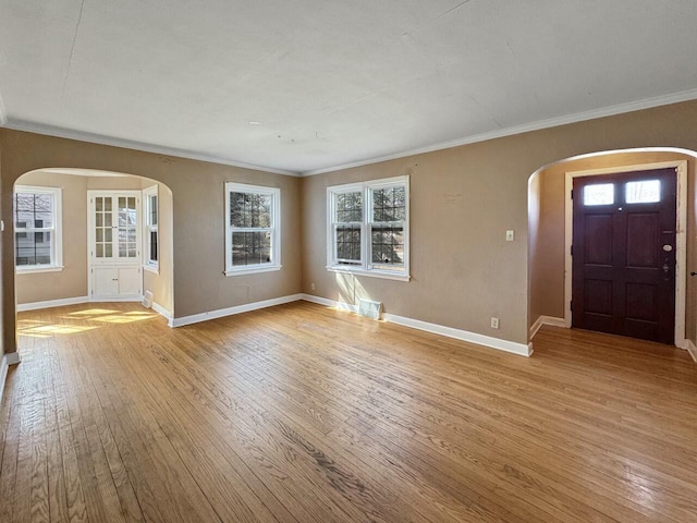 foyer entrance with arched walkways, crown molding, baseboards, and wood-type flooring