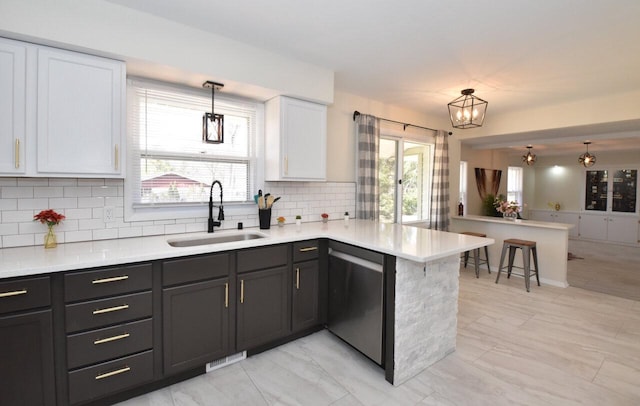 kitchen with dishwasher, light countertops, a peninsula, white cabinetry, and a sink