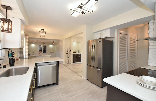 kitchen with pendant lighting, a sink, backsplash, stainless steel appliances, and light countertops