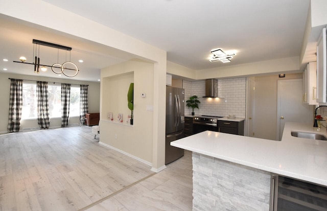 kitchen featuring beverage cooler, a sink, stainless steel appliances, wall chimney range hood, and tasteful backsplash