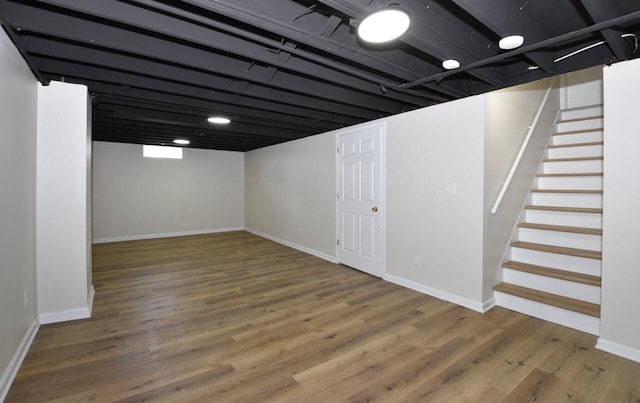 finished below grade area featuring stairway, baseboards, and wood finished floors