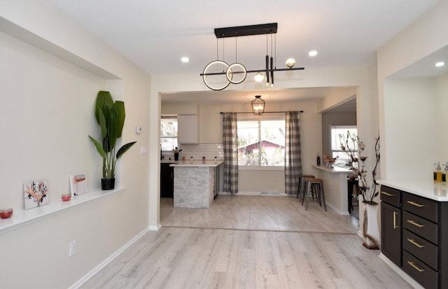 kitchen featuring decorative backsplash, light countertops, baseboards, and light wood-type flooring