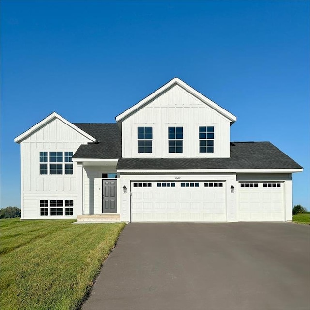 view of front facade featuring a front lawn, aphalt driveway, board and batten siding, roof with shingles, and an attached garage