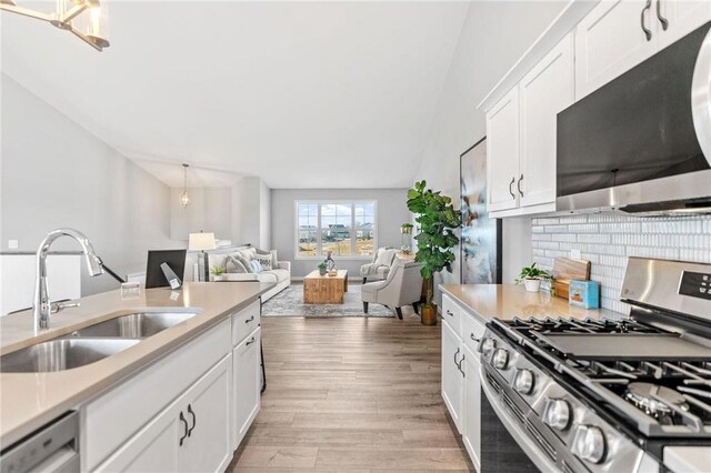 kitchen featuring light countertops, decorative backsplash, light wood-style floors, stainless steel appliances, and a sink