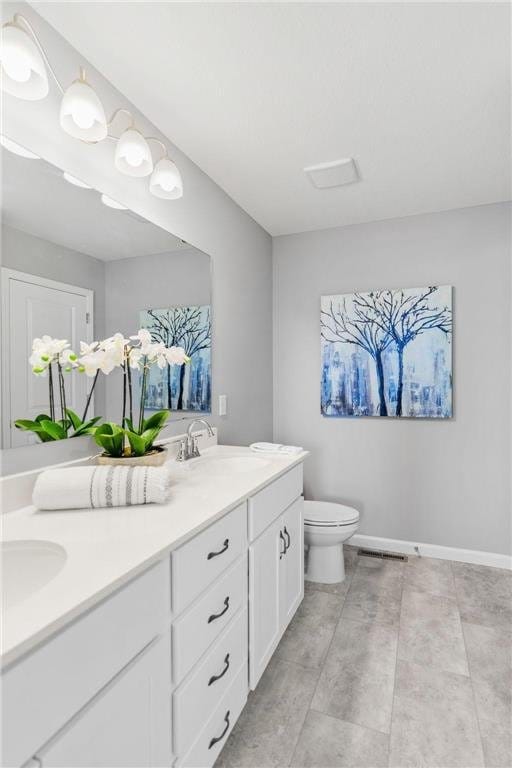 full bathroom with visible vents, toilet, a sink, double vanity, and baseboards