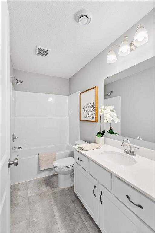 full bath with vanity, washtub / shower combination, visible vents, a textured ceiling, and toilet