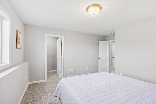 bedroom featuring visible vents, a walk in closet, baseboards, light carpet, and a closet