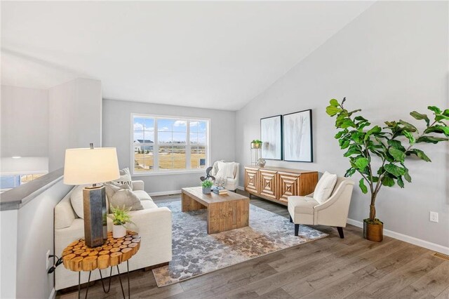 living area with vaulted ceiling, baseboards, and wood finished floors