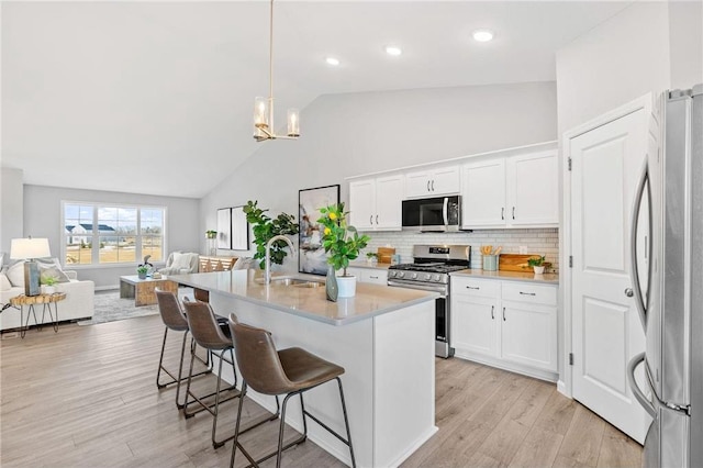 kitchen featuring open floor plan, a breakfast bar, light countertops, appliances with stainless steel finishes, and a sink