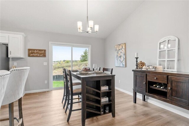 dining space with light wood-type flooring, baseboards, a chandelier, and vaulted ceiling