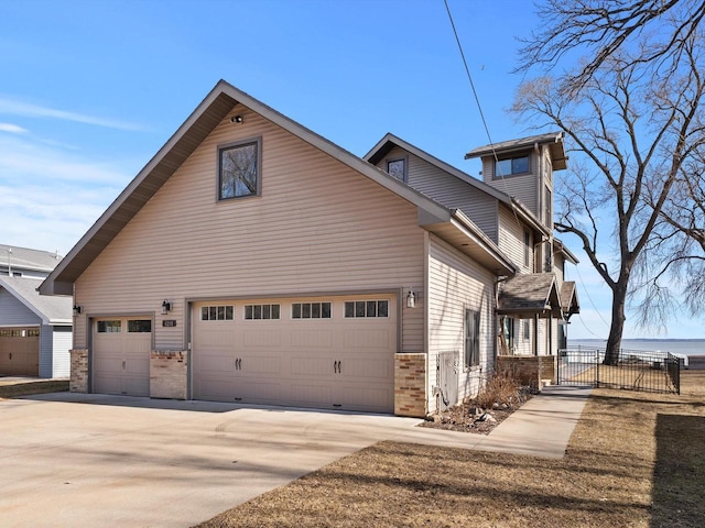 view of side of property featuring a gate, fence, driveway, an attached garage, and brick siding