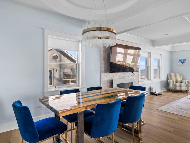 dining area featuring a raised ceiling, wood finished floors, an inviting chandelier, a fireplace, and baseboards