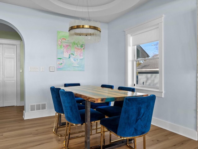 dining space featuring visible vents, arched walkways, baseboards, and wood finished floors