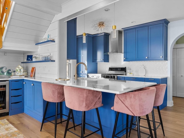 kitchen featuring wall chimney range hood, blue cabinetry, light wood-style floors, and stainless steel gas range