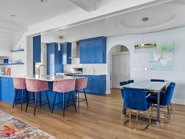 kitchen featuring blue cabinets, electric range, arched walkways, and wall chimney range hood