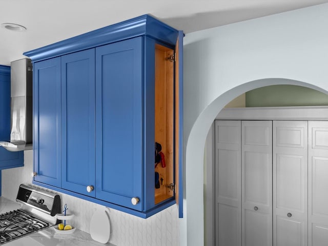 room details featuring arched walkways, stainless steel range with gas stovetop, and blue cabinetry