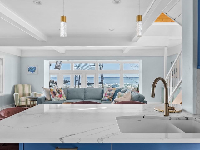 kitchen with beamed ceiling, a sink, light stone counters, open floor plan, and hanging light fixtures