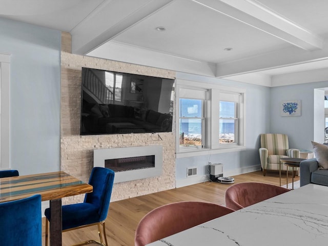 living area featuring visible vents, beamed ceiling, wood finished floors, and a fireplace