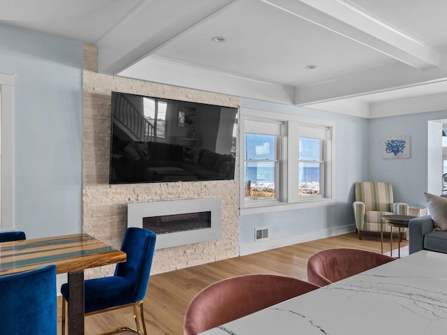 living area with visible vents, beamed ceiling, wood finished floors, a fireplace, and baseboards