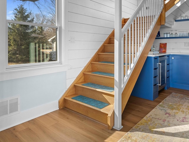 stairway with bar, wood finished floors, visible vents, and wine cooler