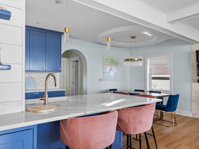 kitchen featuring blue cabinets, light wood-type flooring, a breakfast bar, arched walkways, and light stone countertops