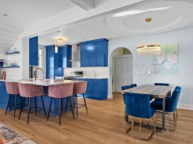 kitchen featuring blue cabinets, arched walkways, stainless steel stove, and wall chimney range hood