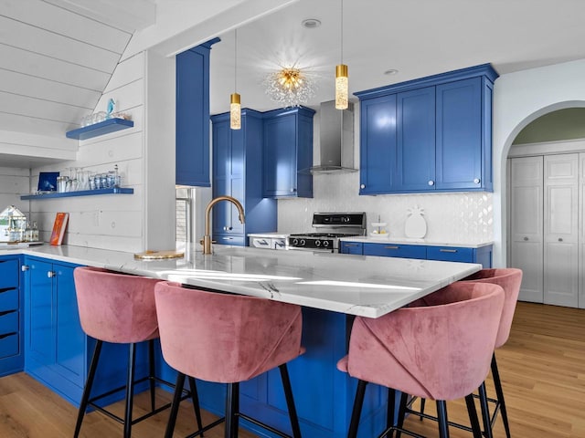 kitchen with blue cabinets, light wood-type flooring, gas range, and wall chimney exhaust hood