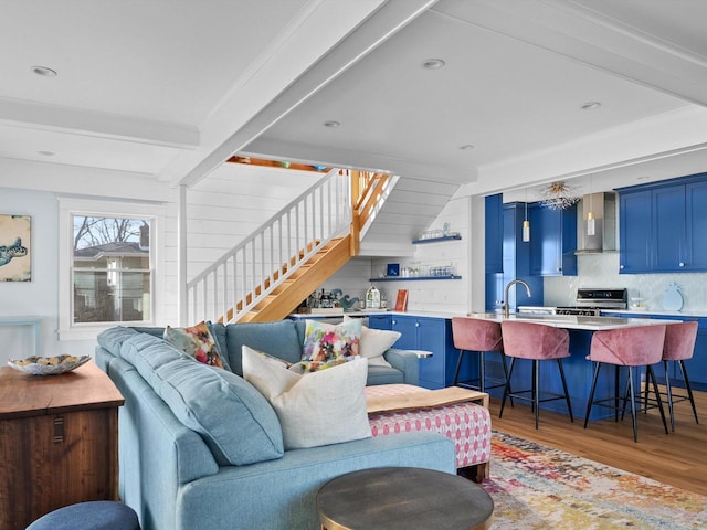 living room with light wood-type flooring, beamed ceiling, and stairs