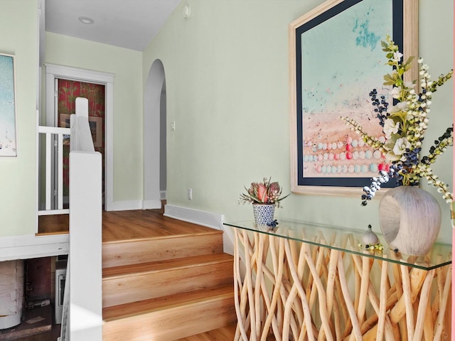 stairway featuring arched walkways, baseboards, and wood finished floors