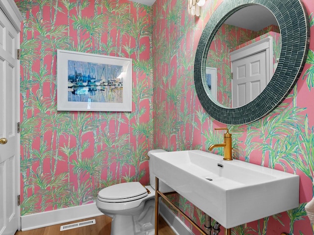 half bath with a sink, visible vents, toilet, and wallpapered walls