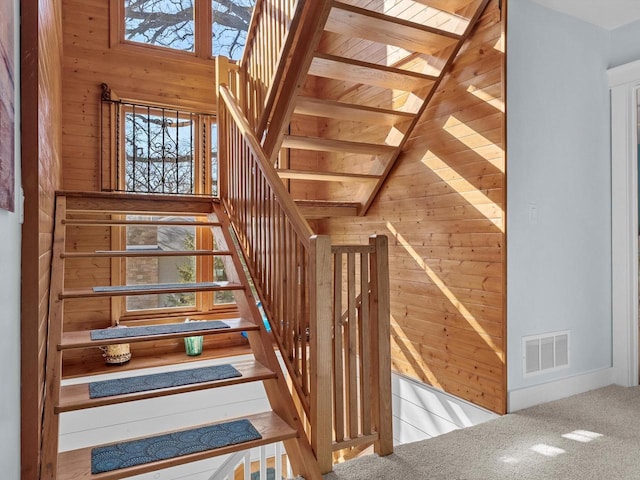 stairs with visible vents, wood walls, and carpet flooring