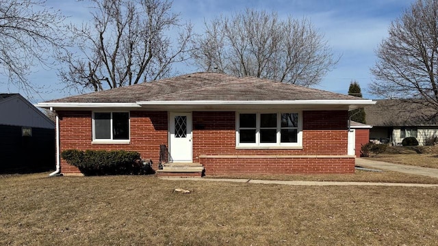 view of front of home with brick siding, a front yard, and roof with shingles