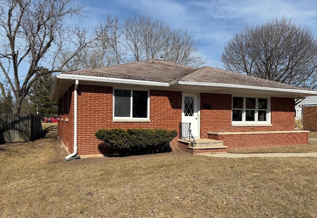 view of front of property featuring brick siding, roof with shingles, a front yard, and fence